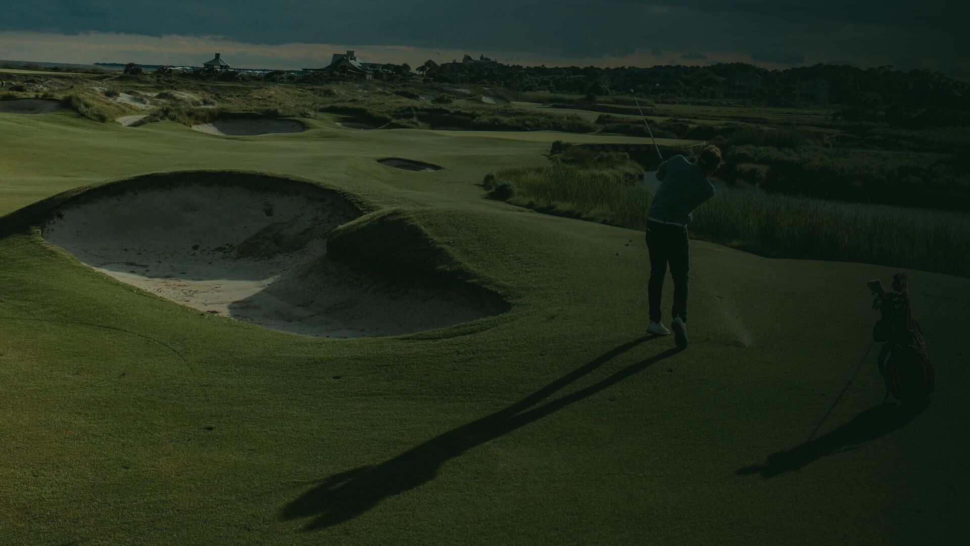 A links golf course at dusk with a golfer finishing their swing